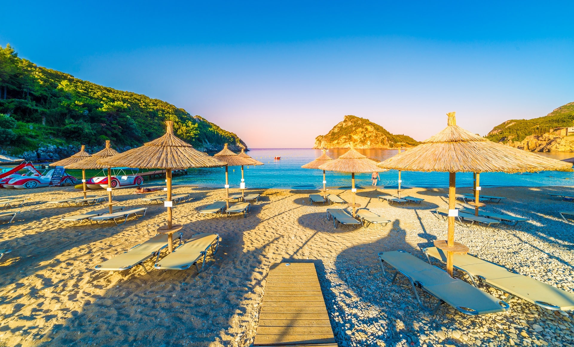 Beach, chairs and umbrellas at sunrise in Paleokastritsa village, Corfu island, Greece